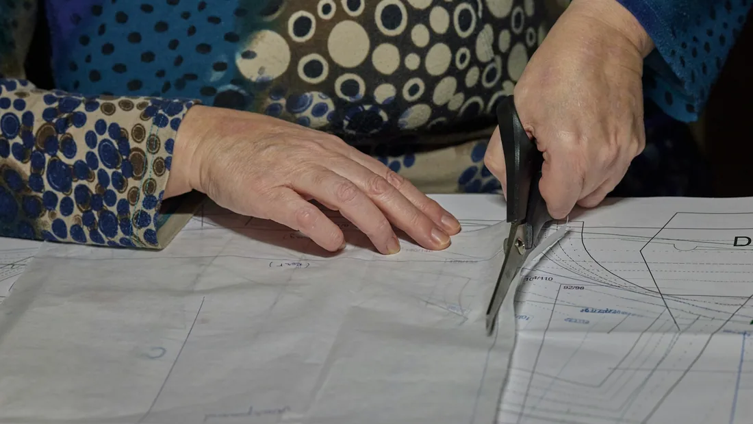 Manos recortando con tijeras un patrón de papel extendido sobre la mesa de corte de un taller de sastrería